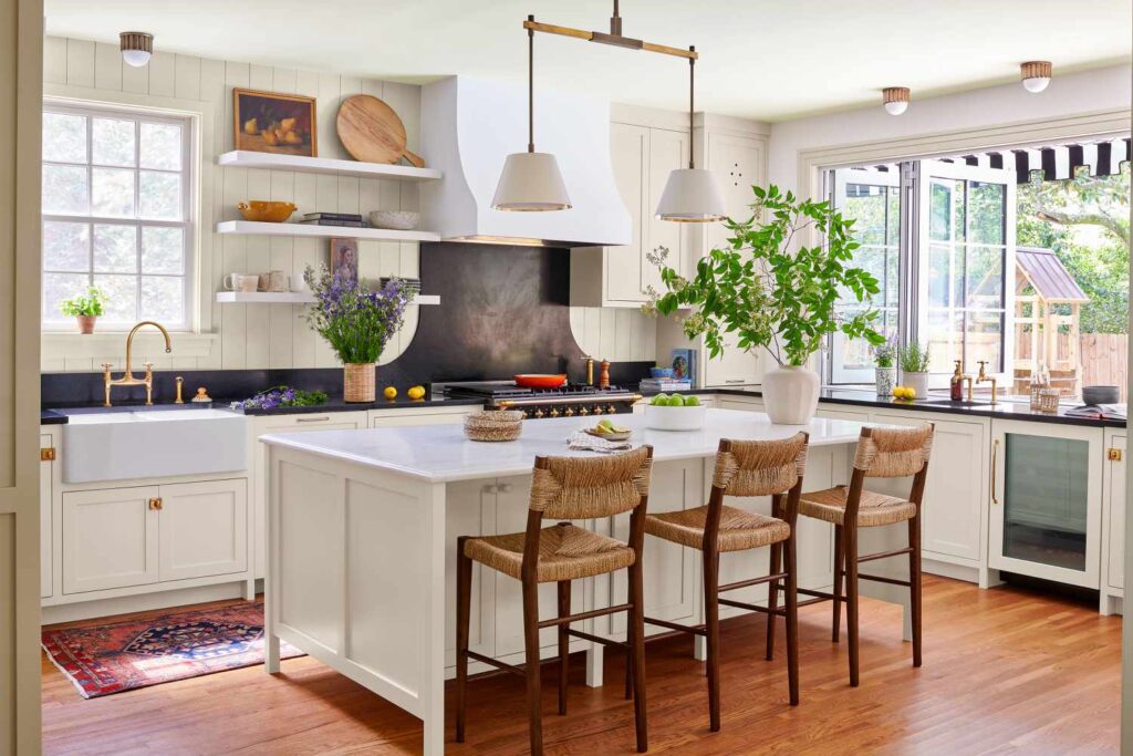 Farmhouse kitchen with white cabinets, natural wood flooring, farmhouse sink, and green plant accents