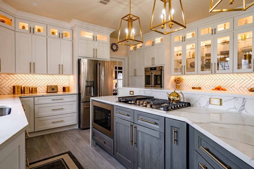 Modern kitchen with white and gray cabinets, gold hardware, marble countertops, and geometric pendant lights