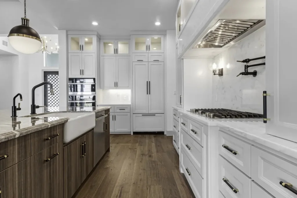 Modern kitchen featuring white upper cabinets, dark wood lower cabinets, farmhouse sink, marble countertops, and black fixtures