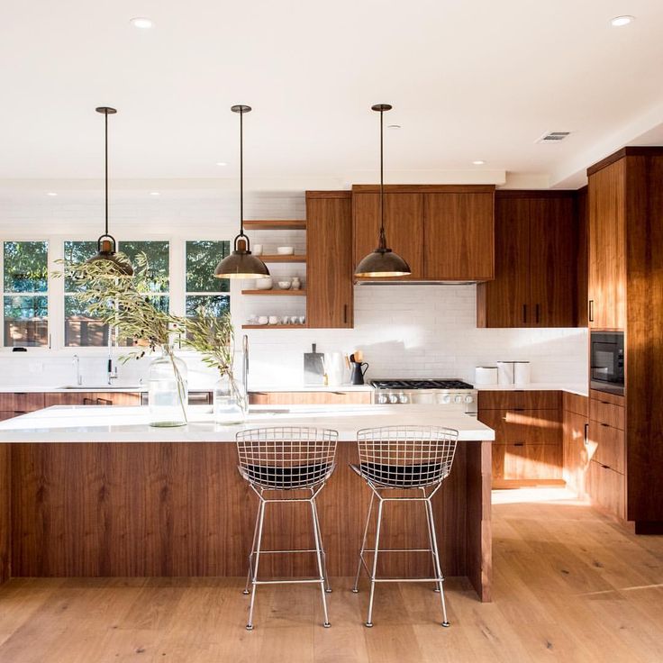 Bright mid-century modern kitchen featuring rich walnut cabinetry, white countertops, pendant lights, and metal bar stools.