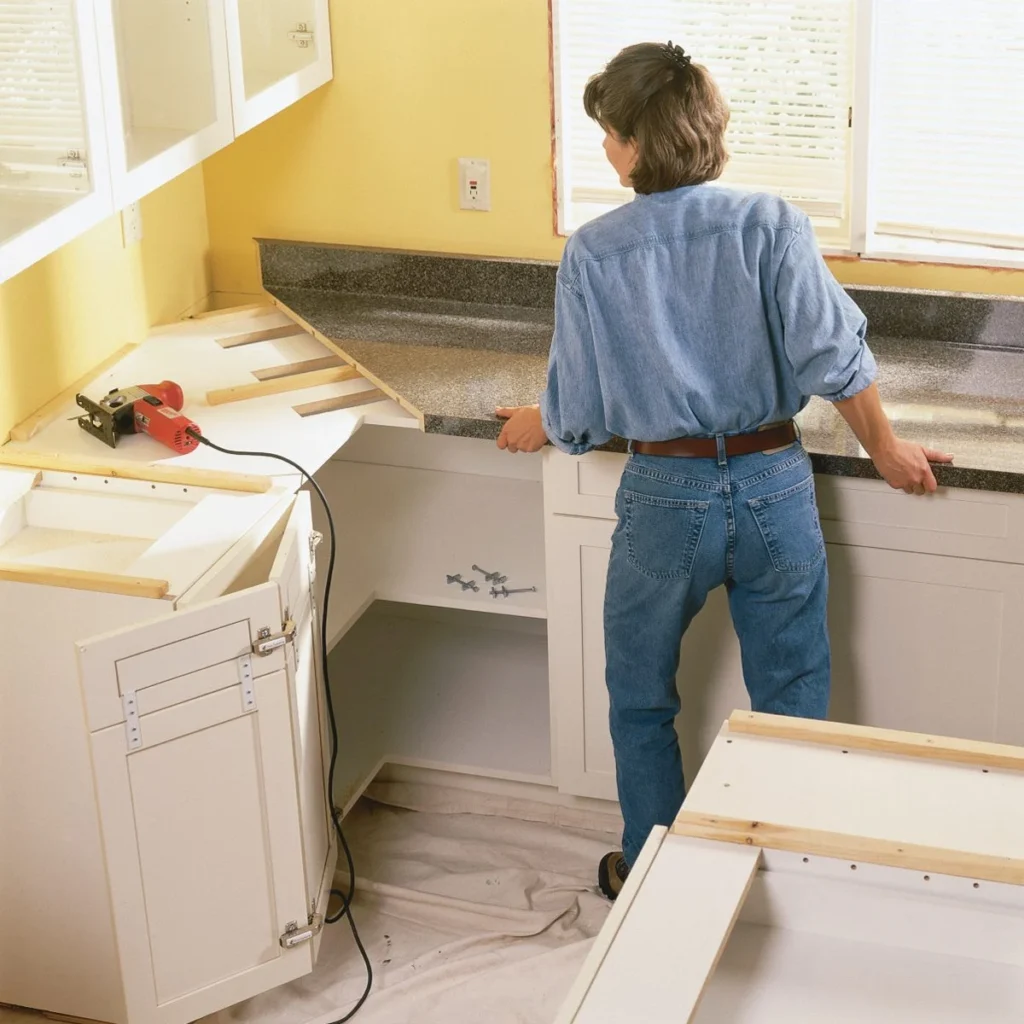 A person fitting a laminate countertop over white kitchen base cabinets, using wooden cleats for support.