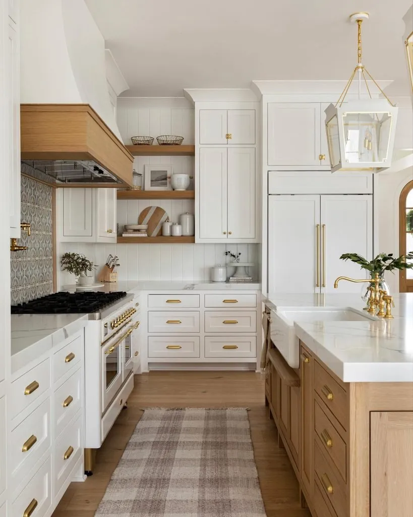 Stylish kitchen with white cabinetry, gold hardware, open wood shelving, and a wood-accented range hood.