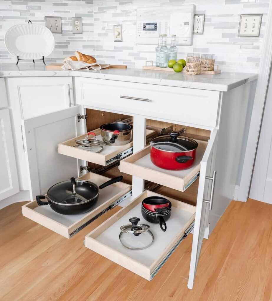 White kitchen cabinet with multiple pull-out drawers storing pots, pans, and lids.