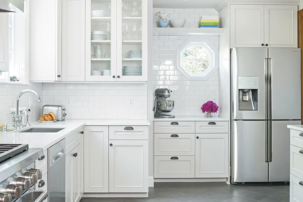 A clean, all-white kitchen featuring custom cabinets, a mixer station, a stainless steel refrigerator, and subway tile backsplash.