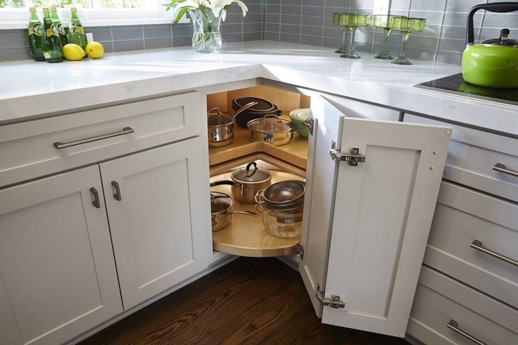 White corner kitchen cabinet with open doors revealing a two-tiered Lazy Susan filled with pots and pans.