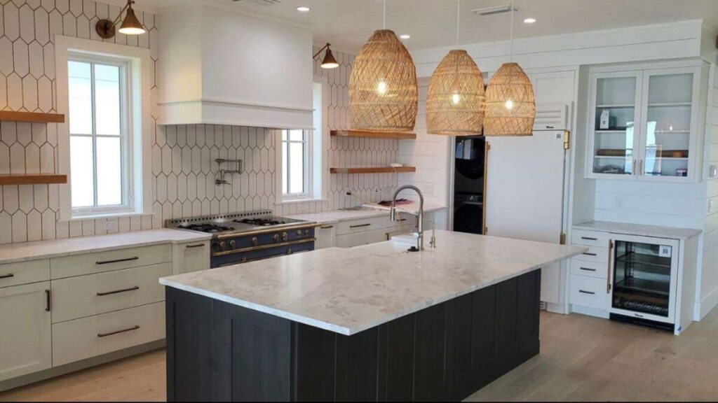 Light coastal kitchen with white vertical tile backsplash, marble countertops, dark island, and rattan pendant lights