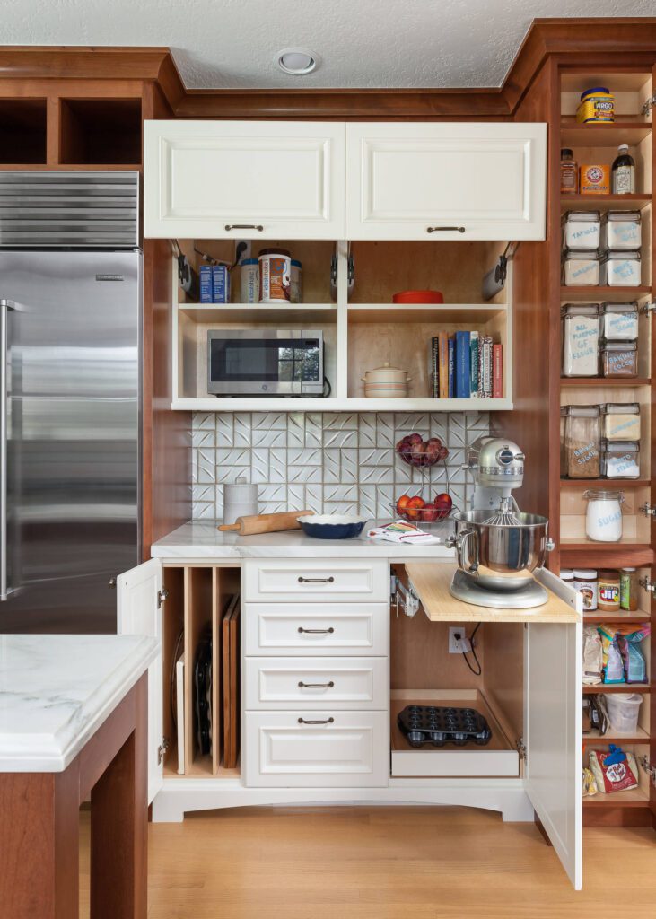 A multifunctional kitchen cabinet featuring an appliance garage with a mixer, microwave shelf, vertical tray storage, and labeled pantry containers.