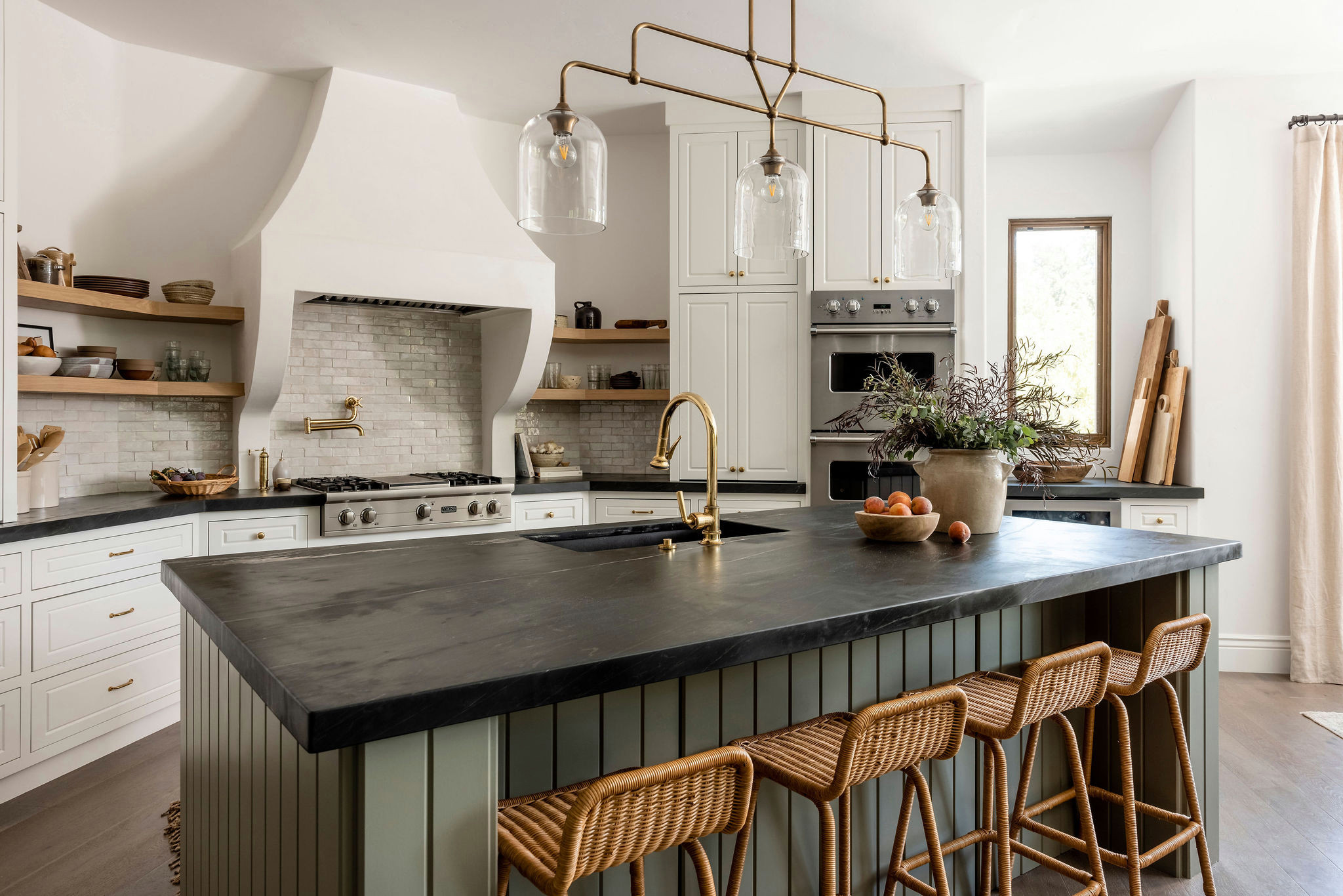 Rustic kitchen with large black stone island, wicker bar stools, and gold fixtures.