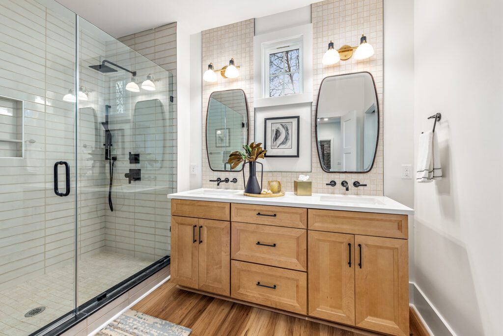 Double sink bathroom vanity with light wood cabinets and modern mirrors