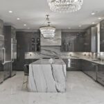 Modern kitchen featuring glossy gray cabinets, dramatic marble island, and crystal chandeliers