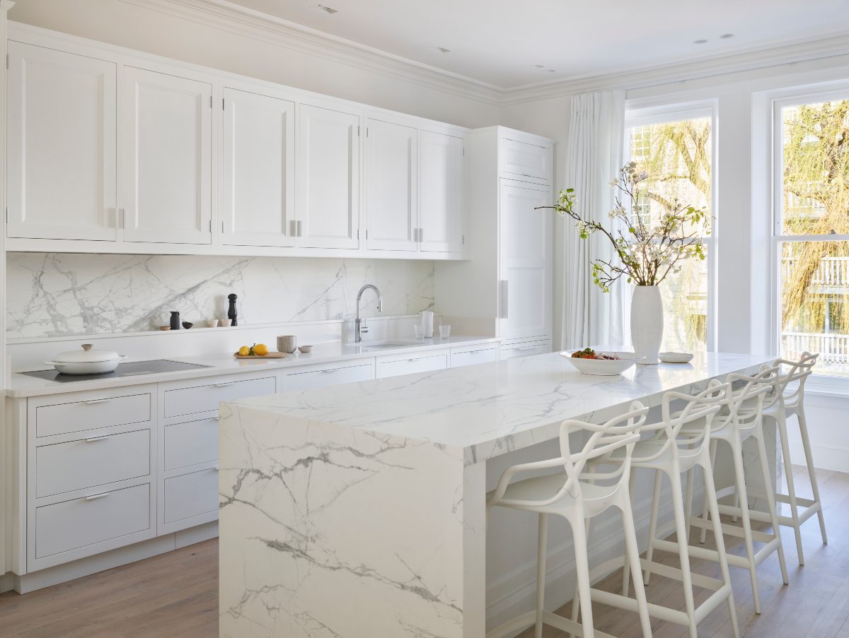 Modern kitchen featuring white cabinetry, marble backsplash, and a waterfall marble island with stylish white bar stools