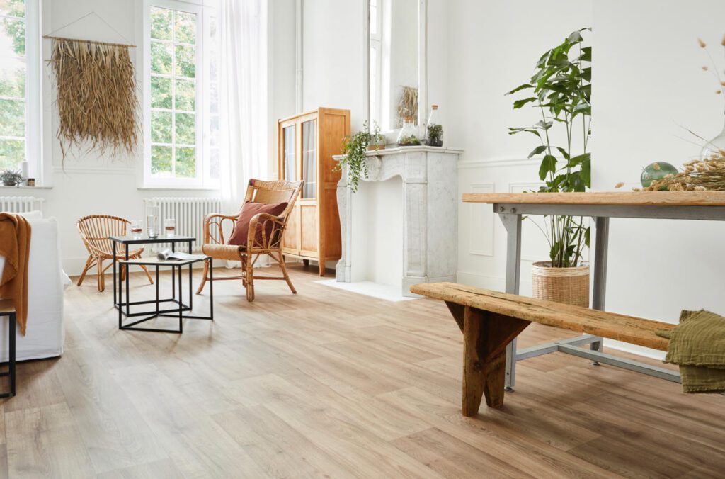 A bright living room with light brown oak-look vinyl flooring, rattan furniture, and natural decor.