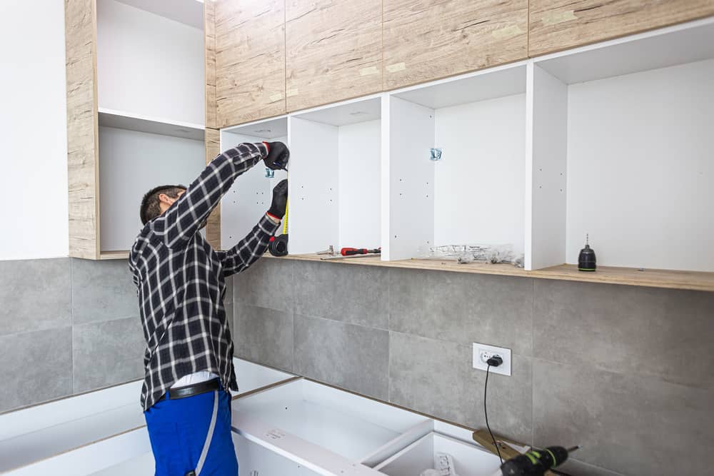 Man installing upper kitchen cabinets with tools and tape measure