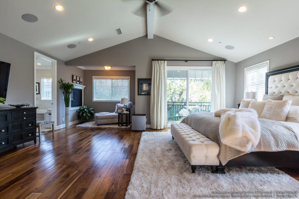  A spacious master bedroom with natural walnut hardwood flooring, luxurious bedding, and a private sitting area.