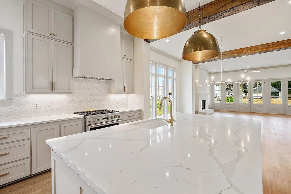 Spacious kitchen featuring quartz countertops, neutral cabinets, brass pendant lighting, and wooden ceiling beams