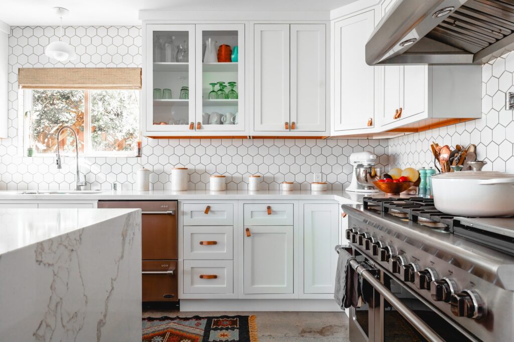 White kitchen with hexagonal tile backsplash, leather cabinet pulls, and stainless steel range