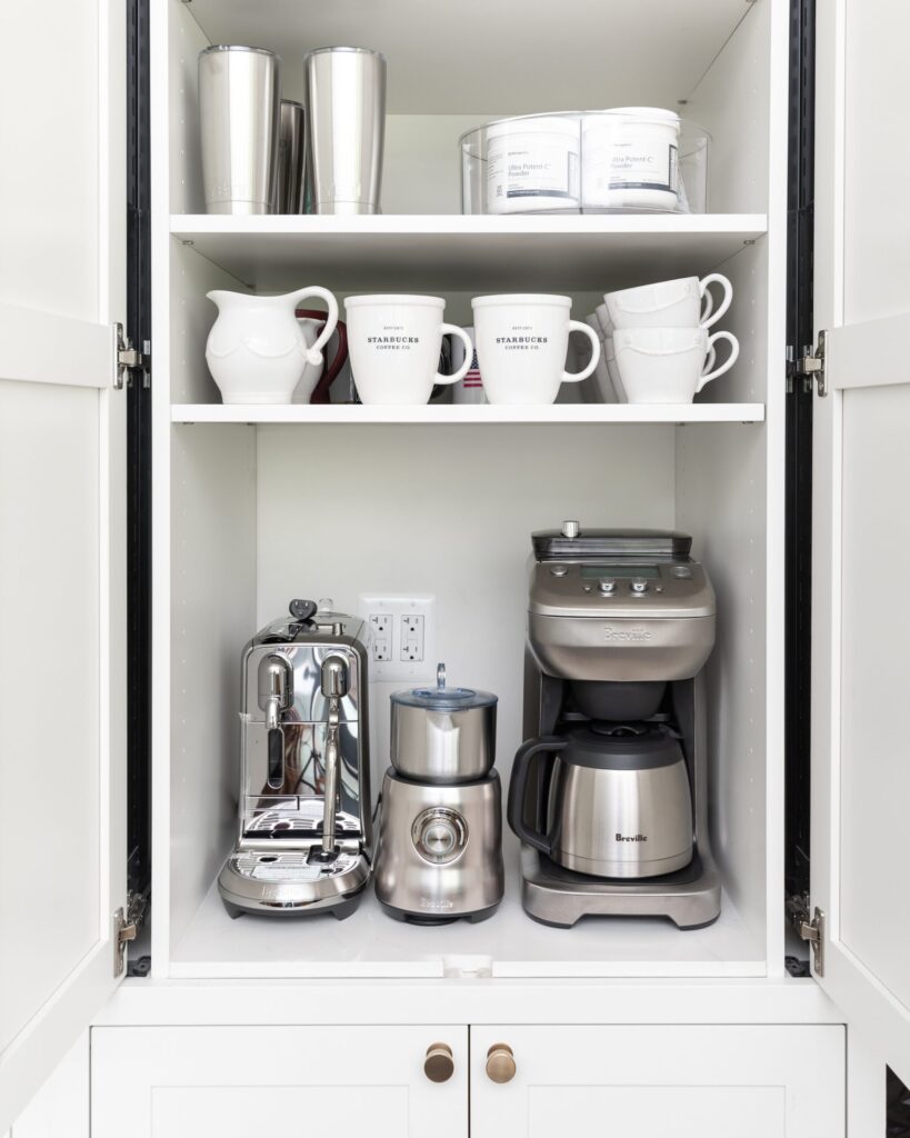 Organized kitchen cabinet with coffee makers, mugs, and stainless steel tumblers
