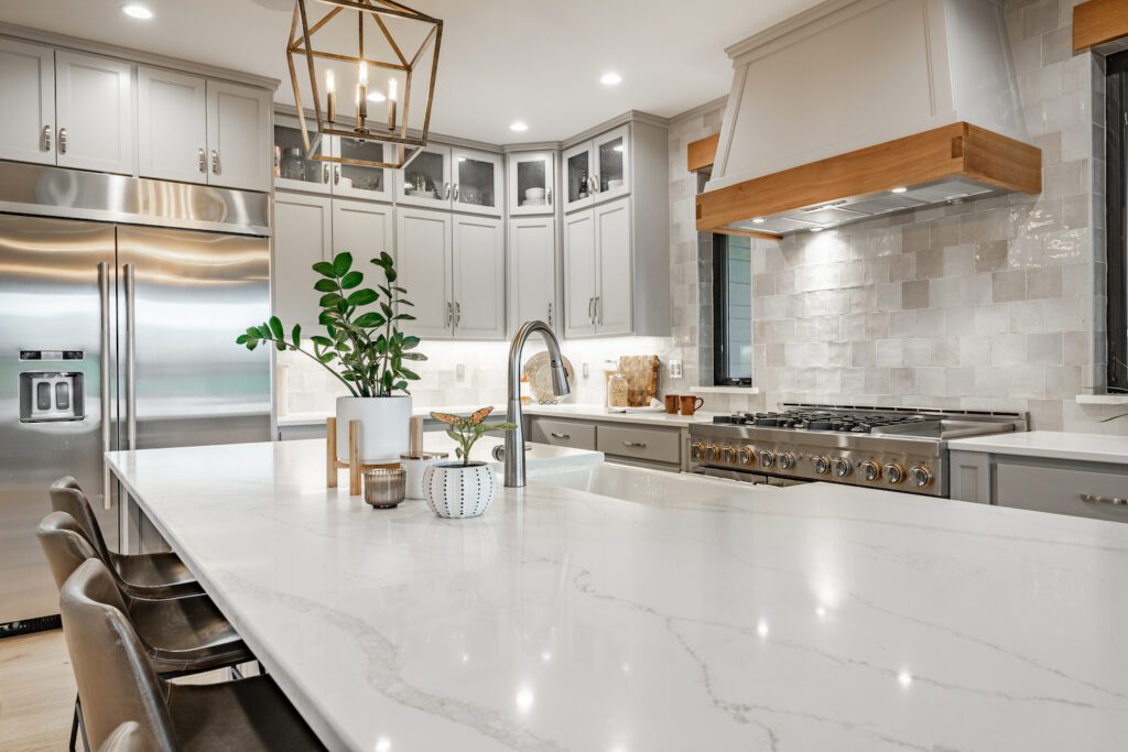 Contemporary kitchen with sleek white quartz countertops, gray cabinets, stainless steel refrigerator, and a large gas range