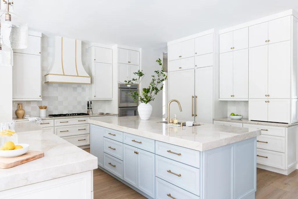 Luxurious kitchen featuring white cabinets, light blue island, marble countertops, and gold hardware