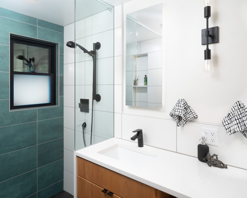 Modern bathroom with glass shower, teal wall tiles, and single-sink vanity