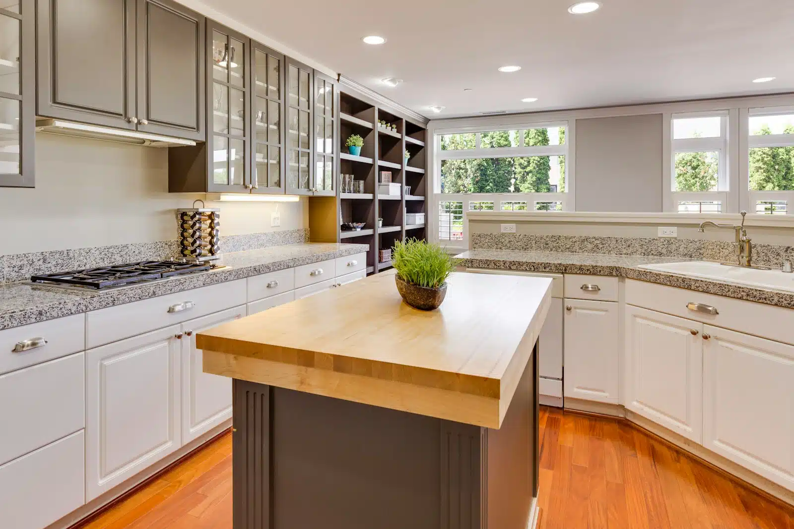 Spacious kitchen with granite countertops, glass-front upper cabinets, a wood butcher block island, and hardwood flooring.