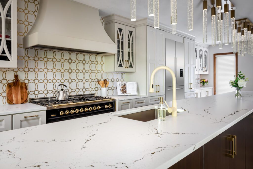 Luxury kitchen with white marble countertops, gold fixtures, and a stylish geometric backsplash.