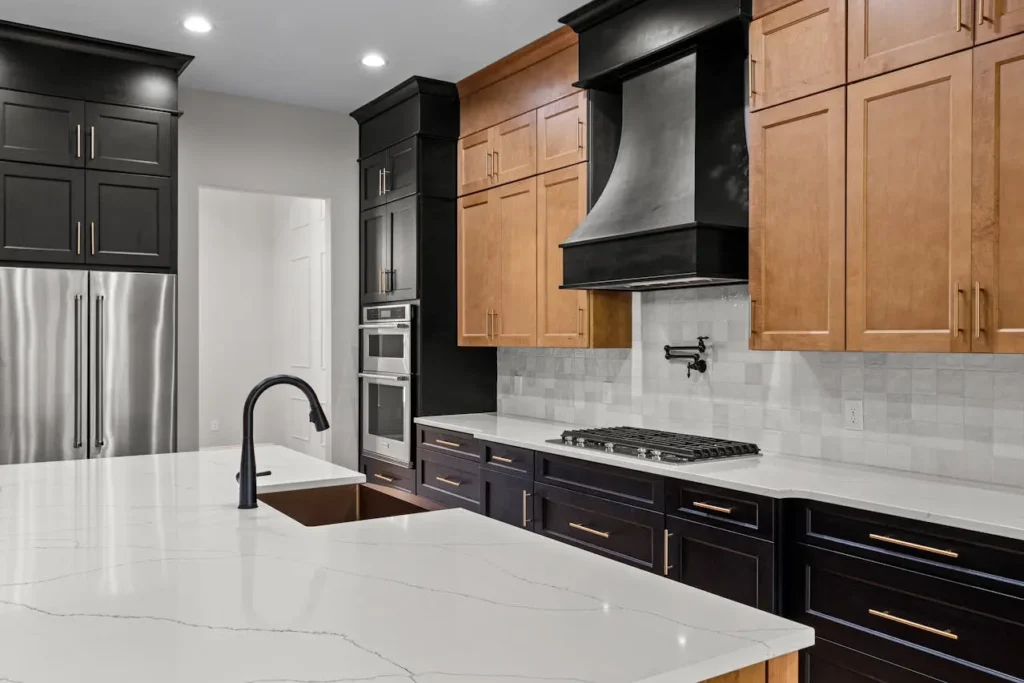 Stylish kitchen featuring two-tone black and wood cabinets, white quartz countertops, black faucet, and stainless steel appliances