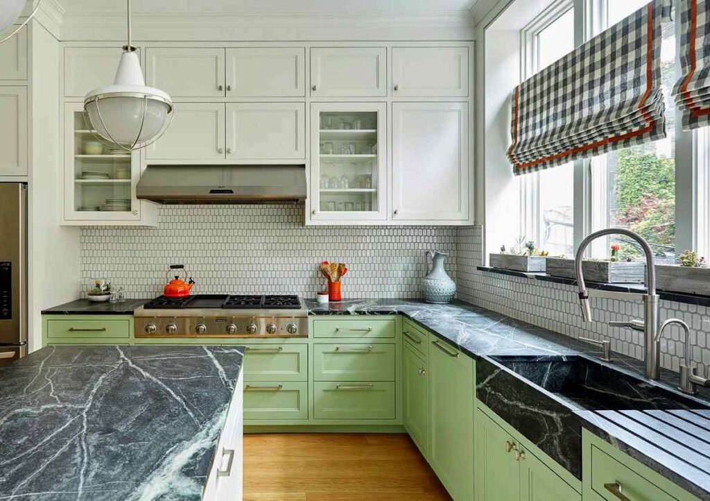 Kitchen with mint green lower cabinets, white upper cabinets, black marble countertops, and checkered roman shades.