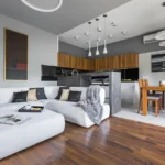 A stylish modern living and kitchen area featuring dark wood flooring, white tile, and minimalist furniture.