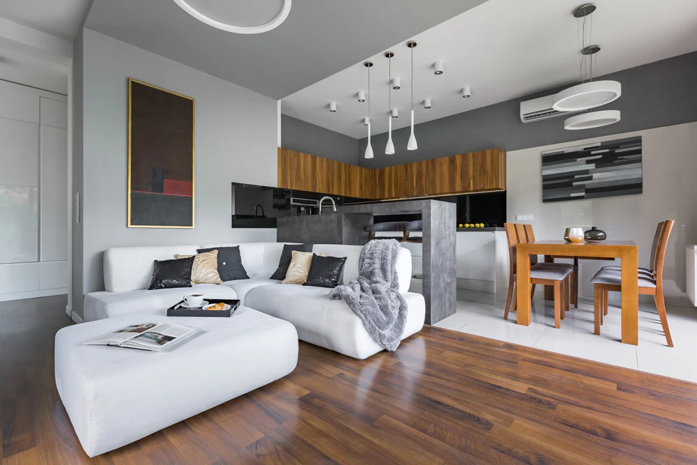 A stylish modern living and kitchen area featuring dark wood flooring, white tile, and minimalist furniture.