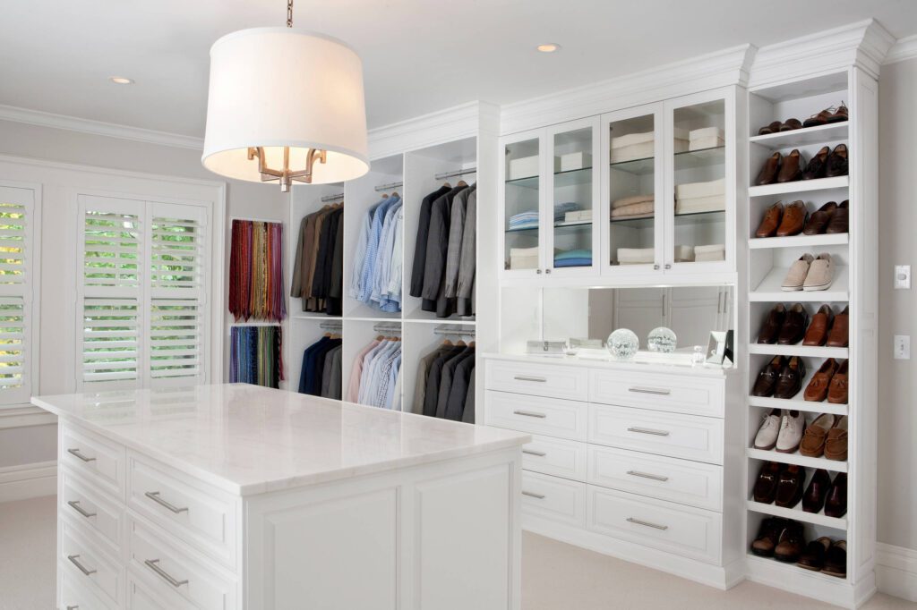 White walk-in closet featuring an island with drawers, shoe shelves, and hanging space for suits and shirts