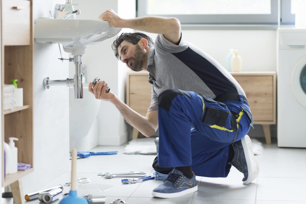 Plumber repairing a bathroom sink with tools on the floor