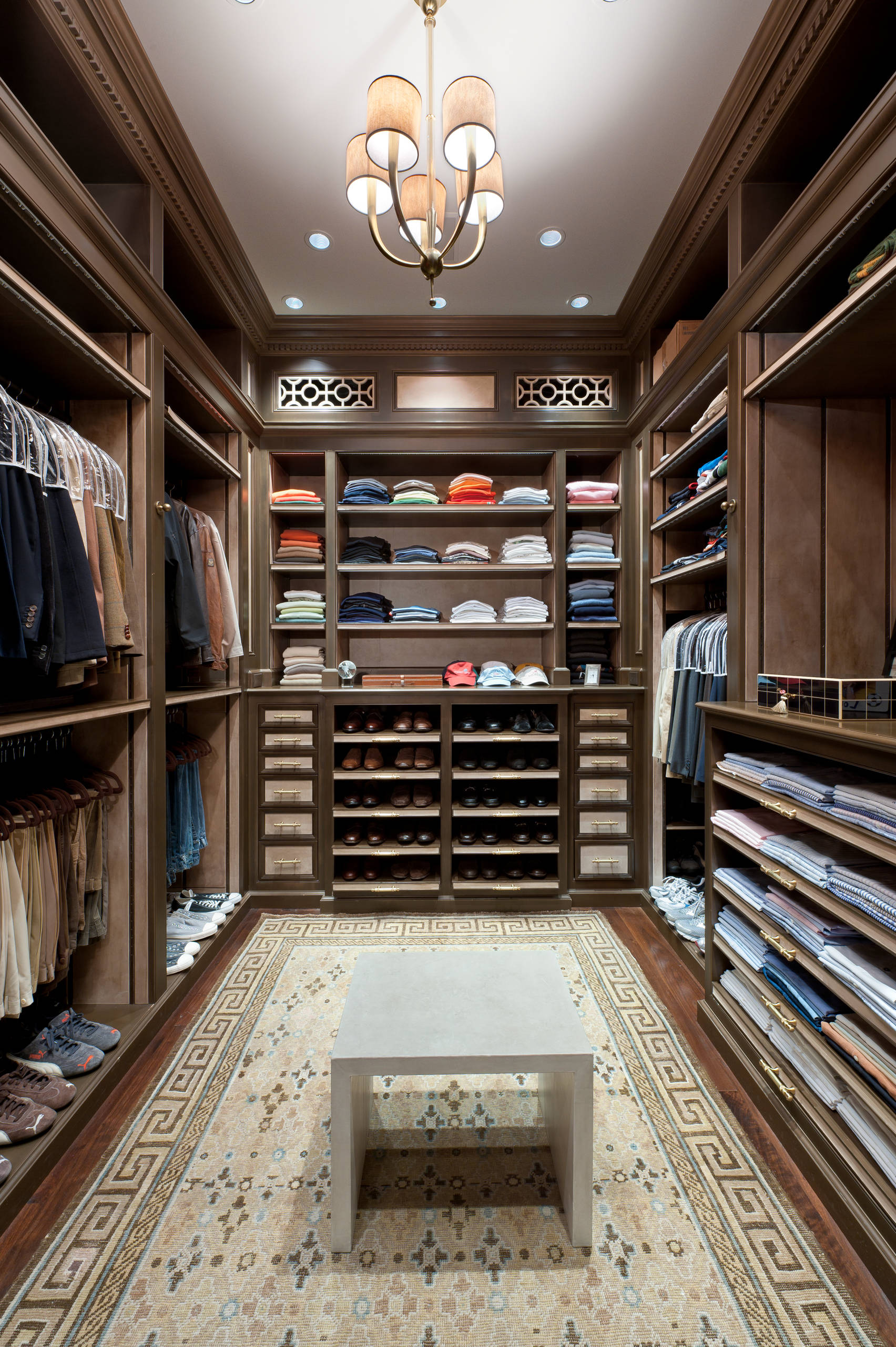 Luxurious walk-in closet with custom wood cabinetry and chandelier