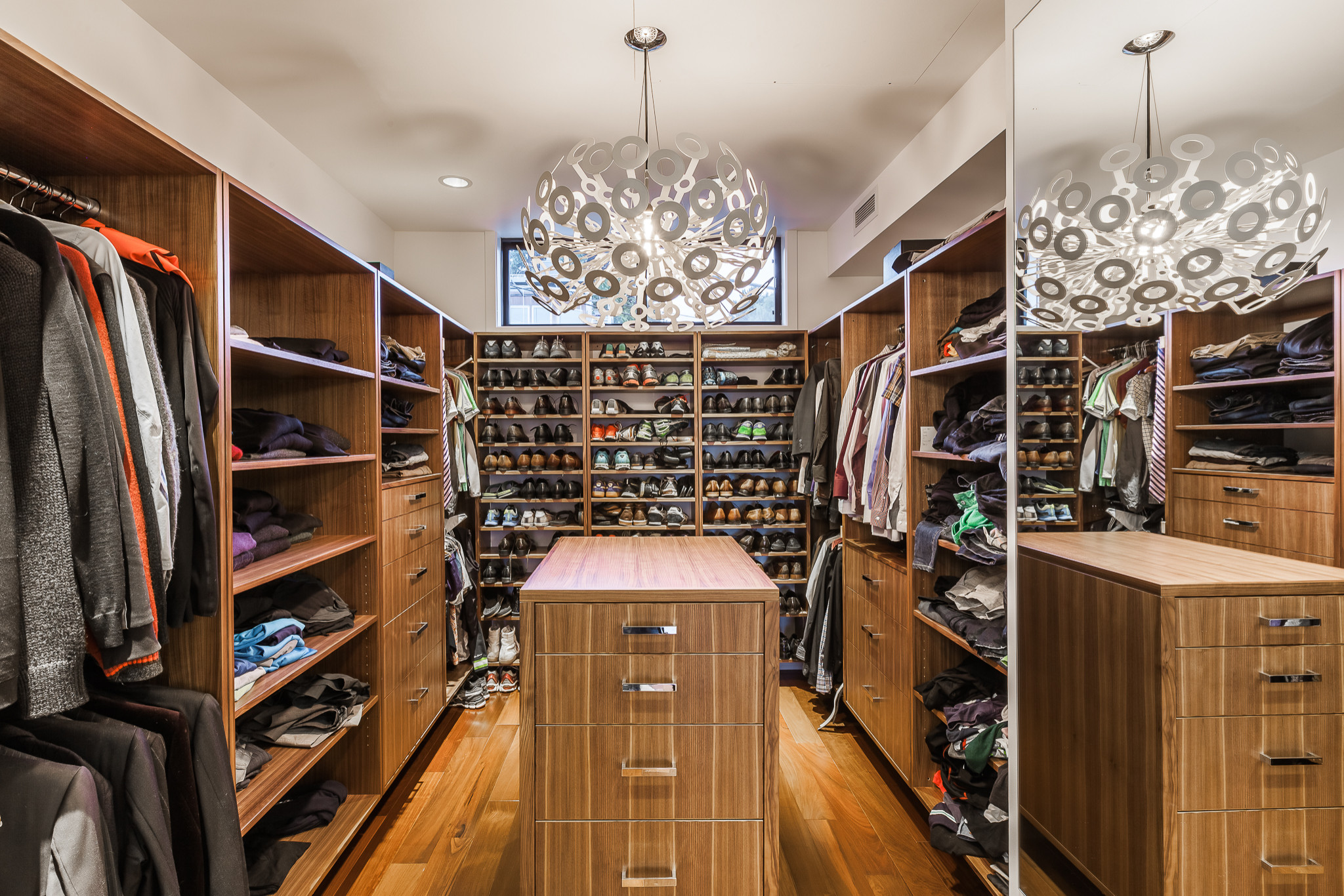 Modern walk-in closet with wooden shelves, island drawers, and contemporary chandelier