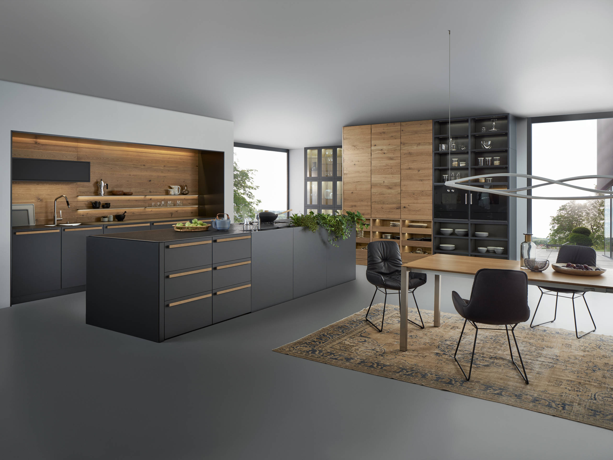 Modern minimalist kitchen with matte black cabinetry, wood accents, and integrated dining area featuring sleek contemporary furniture.