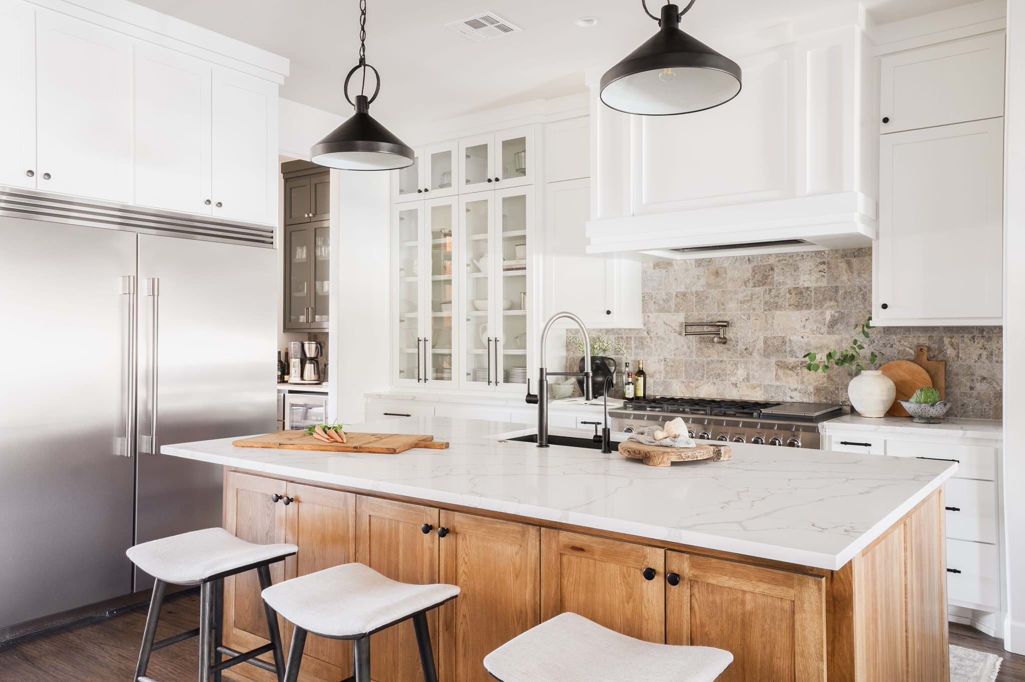 Bright modern kitchen with white cabinets, wood island, marble countertop, and stainless steel refrigerator.