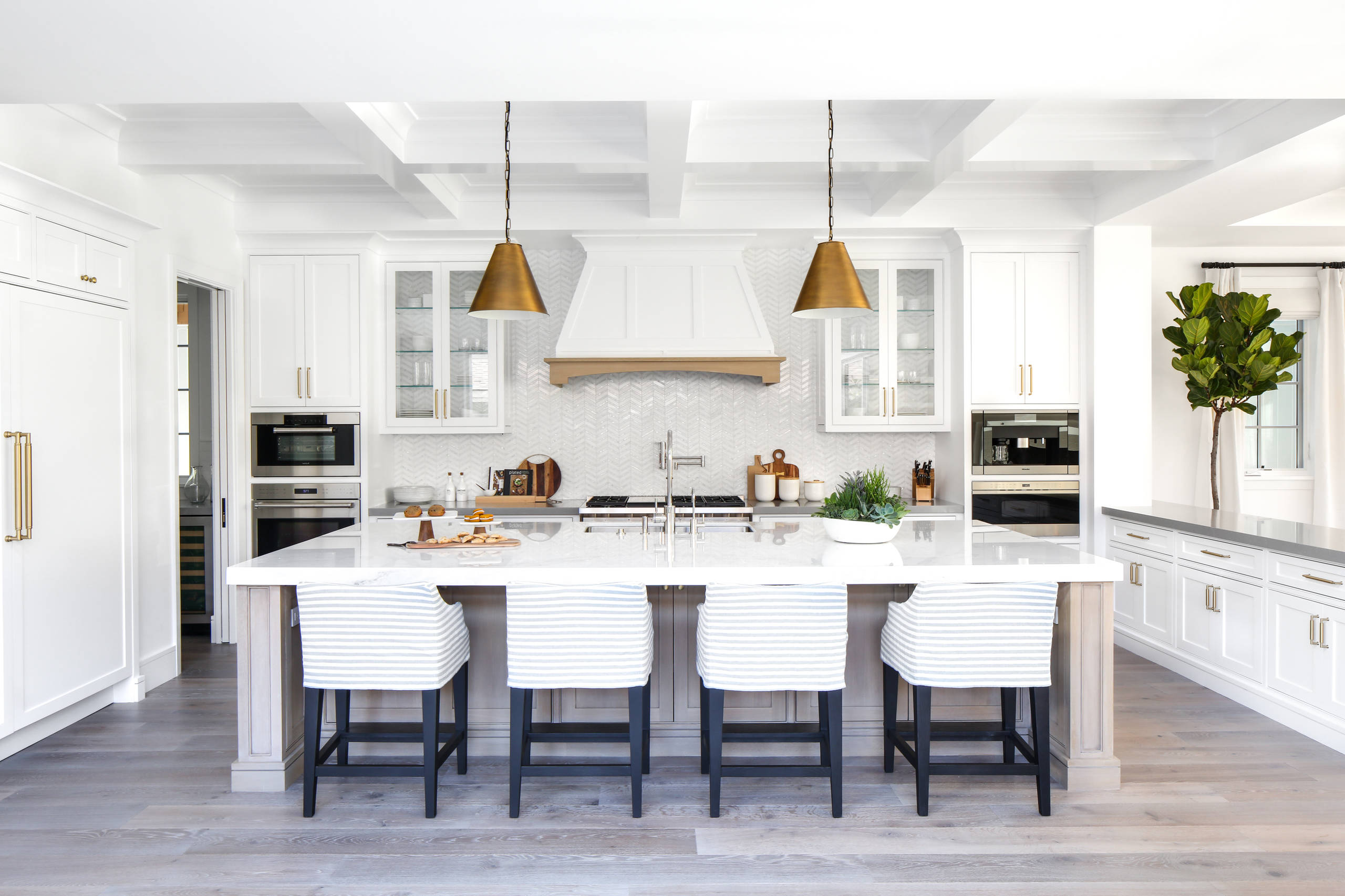 Bright modern kitchen with a large white island, pendant lighting, and upholstered bar stools in a clean, airy design.