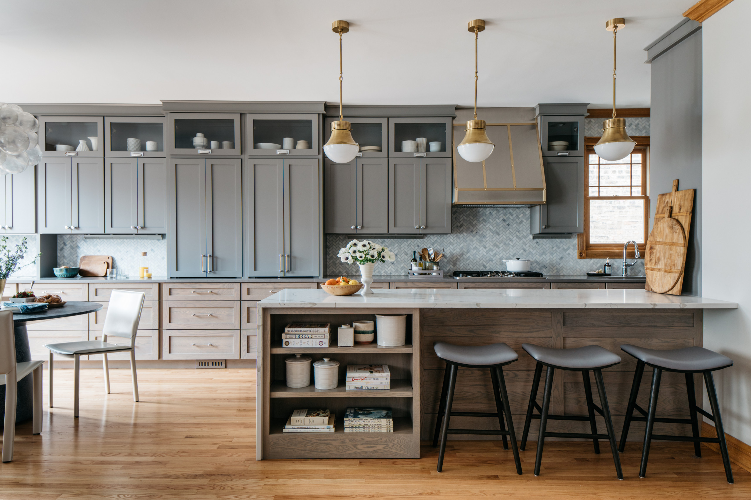 Modern kitchen with gray cabinetry, marble island, brass pendant lighting, and wooden flooring.