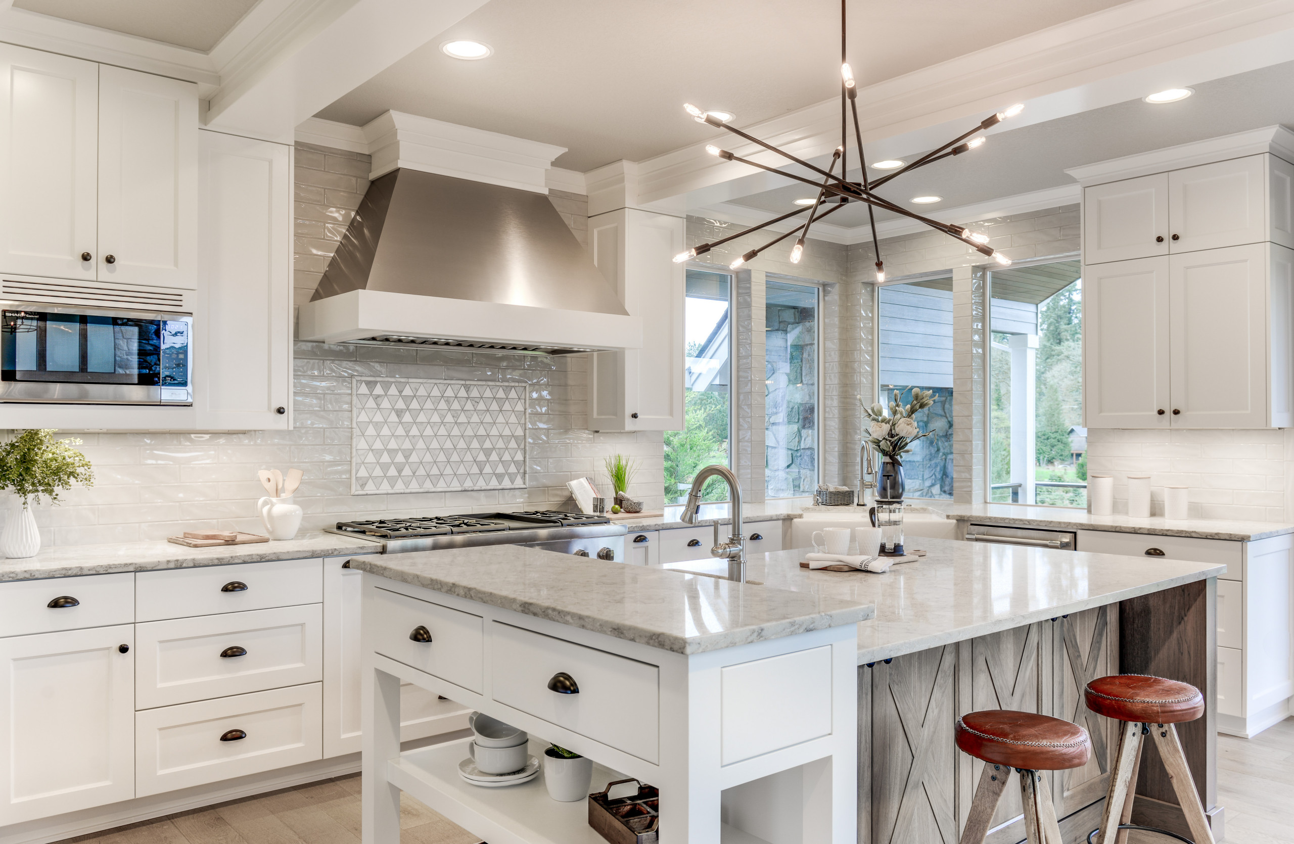 Bright white kitchen with marble countertops, modern lighting fixture, and stainless-steel appliances.