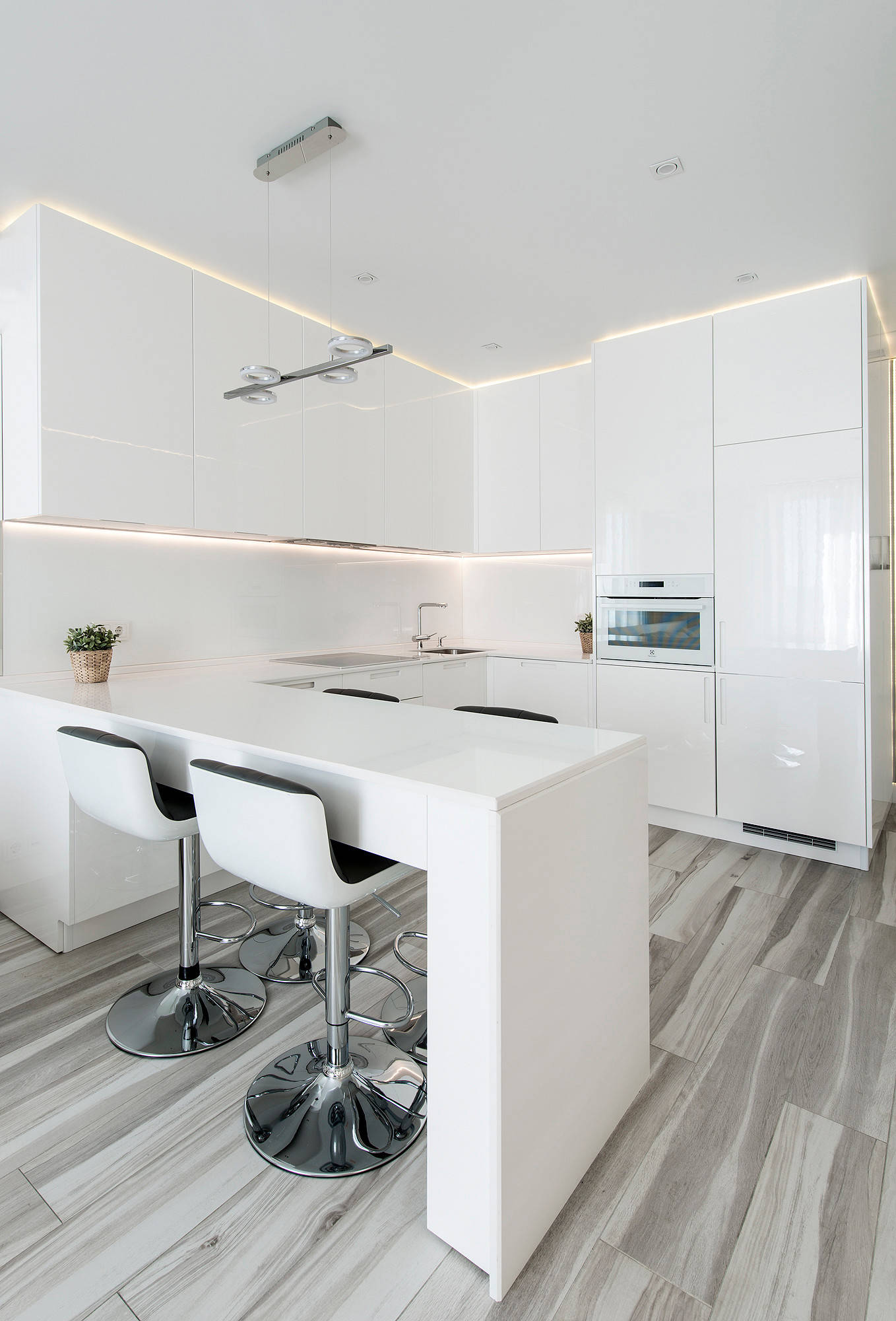 Minimalist white kitchen with glossy cabinets, modern bar stools, and soft LED lighting.