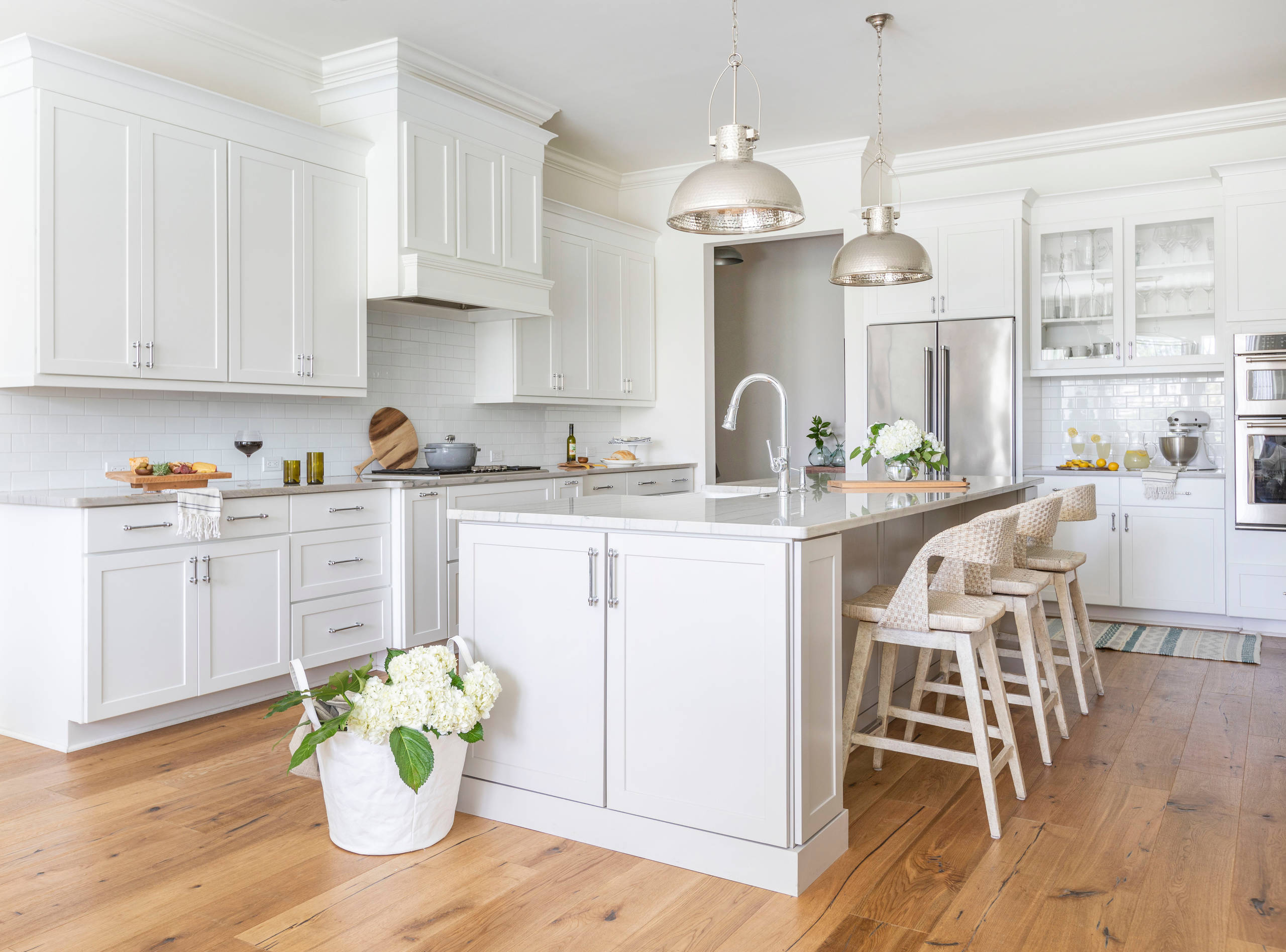 Bright white kitchen with large island, pendant lighting, and wooden floors for a clean, airy look.
