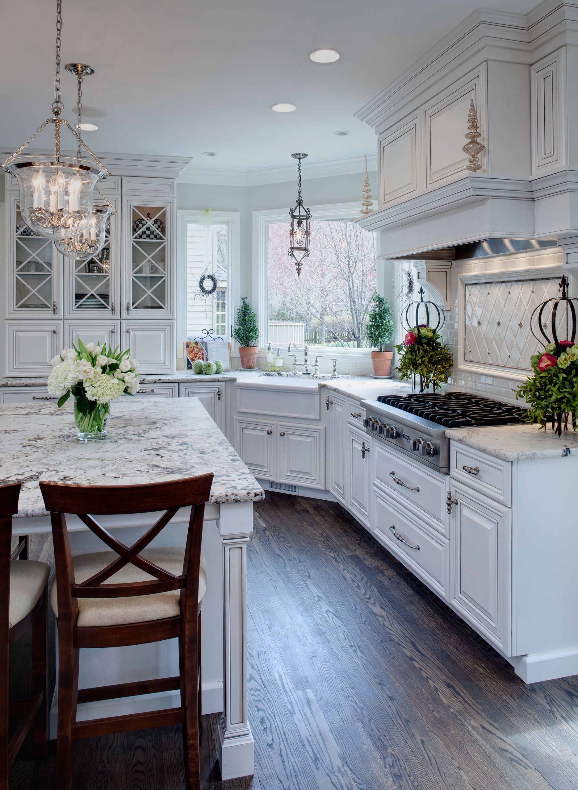 Elegant traditional kitchen with white cabinetry, marble countertops, and ornate pendant lighting.
